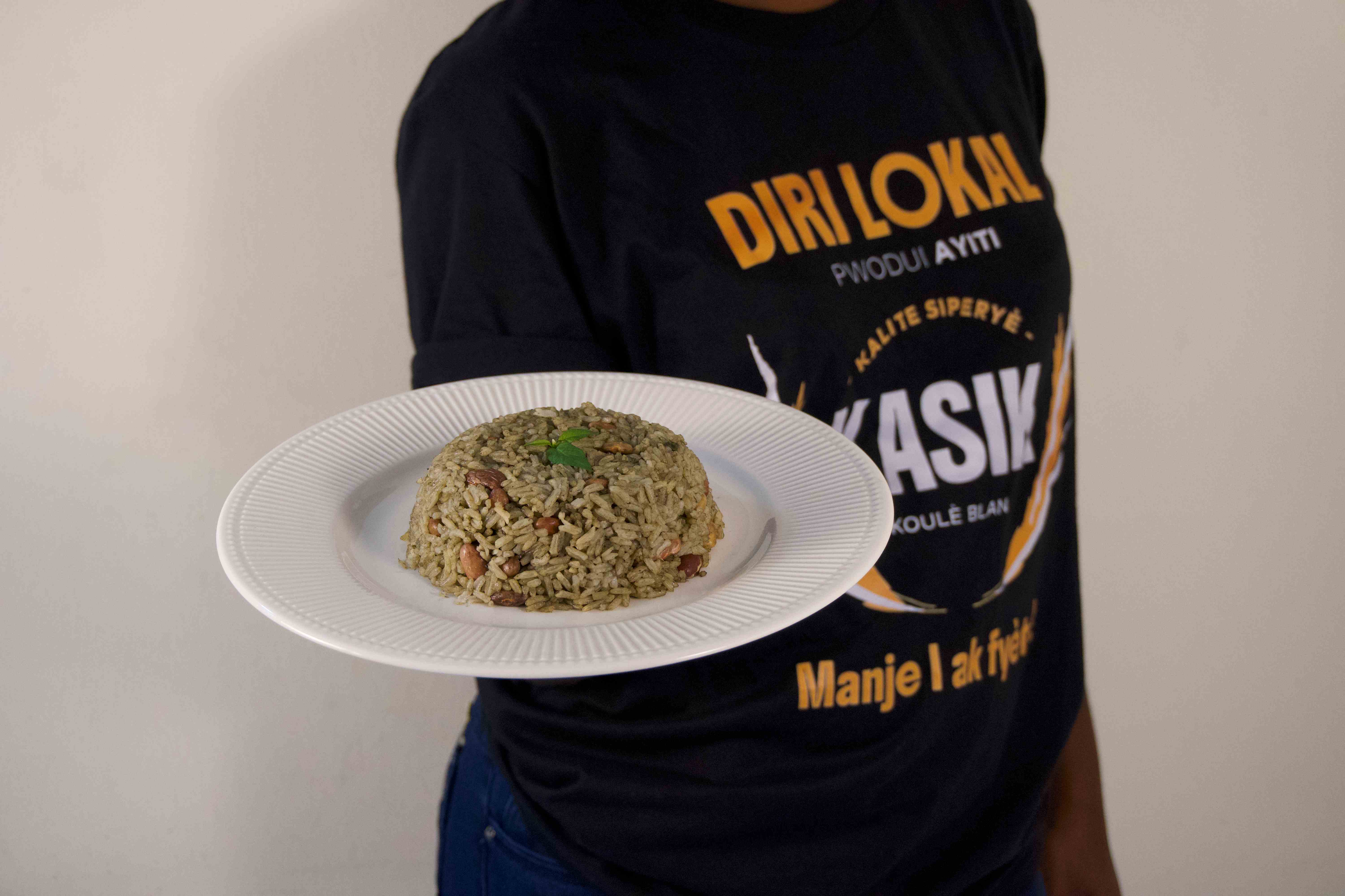 Assiette de riz djon-djon Diri Kasik tenue par une personne en t-shirt Kasik
